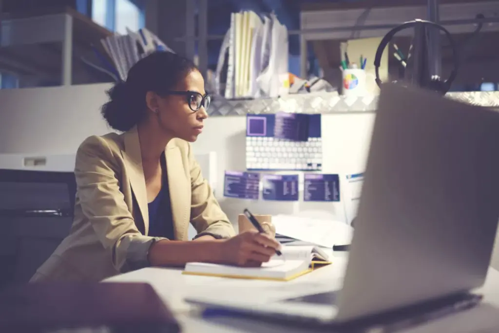 A healthcare administrator writes in a notebook at her desk while studying a computer screen.