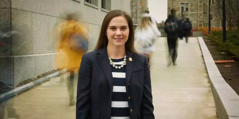 A healthcare student stands on campus as people walk behind her.