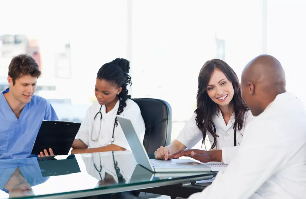 A diverse group of healthcare professionals speak to each other around a conference table.