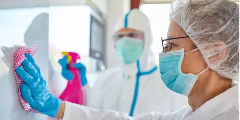 Healthcare workers in masks and hazmat suits clean a wall.