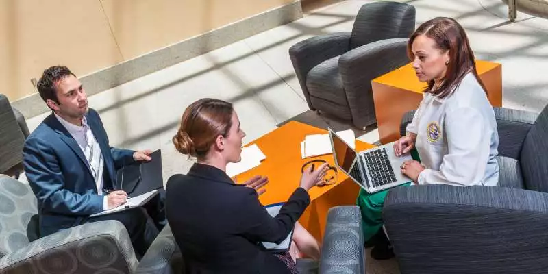 A group of healthcare administrators speak to one another in the lounge area of an airy building.