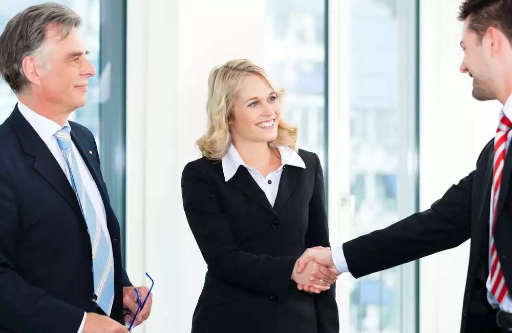 Three health administrators smile at one another as two of them shake hands.