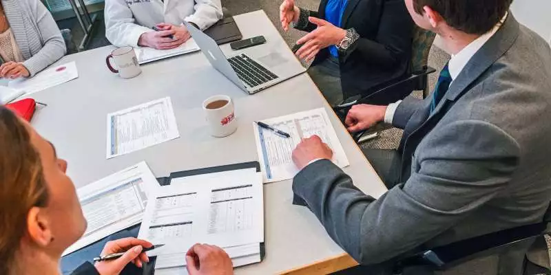 A group of health administrators gather around a conference table with many documents on it.