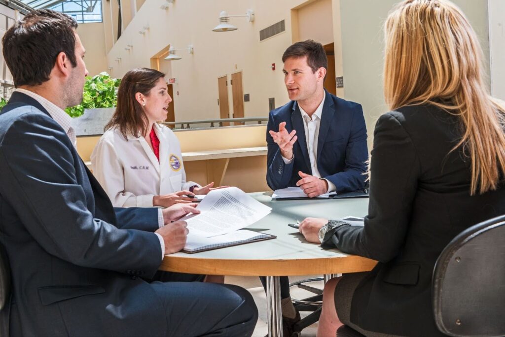 A group of healthcare administrators meets with a healthcare provider in an office common space.