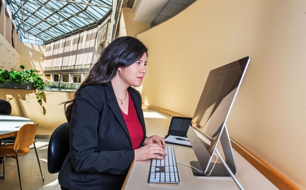A woman in business attire types on a desktop computer in a bright, modern study area.